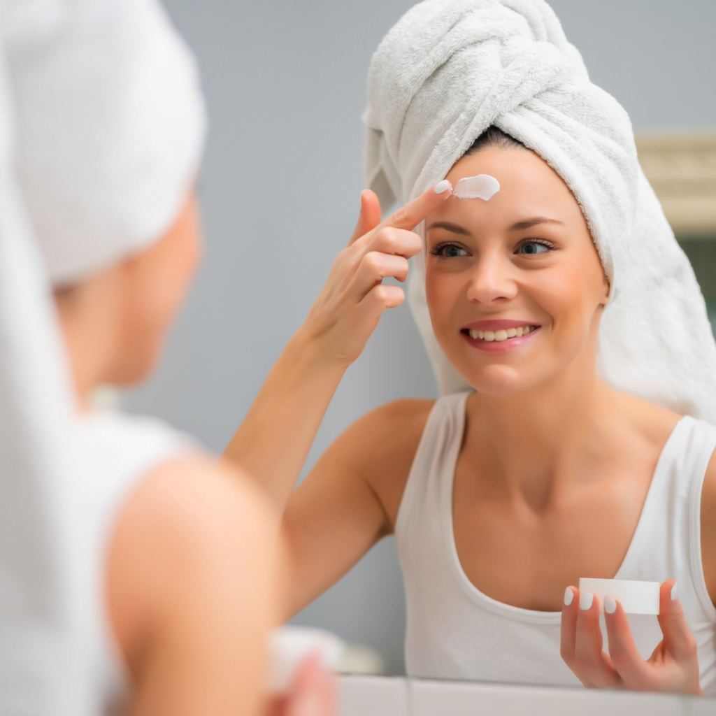nasmejana žena ispred ogledala nanosi na lice kremu sa zaštitnim faktorom