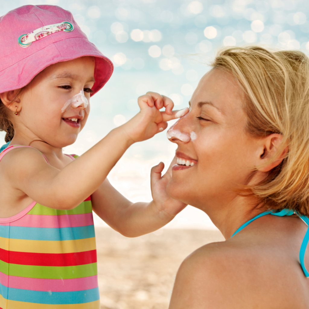 zaštita kože od sunca izuzetno je važna za decu i osobe sa svetlom puti zbog čega devojčica sa šeširom i njena mama na plaži jedna drugoj nanose na lice kremu sa zaštitnim faktorom