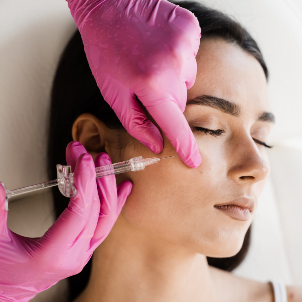 žena leži dok doktor aplicira injekciju hijaluronskih filera u njen obraz tokom tretmana podmlađivanja lica hijaluronskim filerima. Hijaluronsli fileri izuzetno su efikasni i u tretmanima za podizanje jagodica.