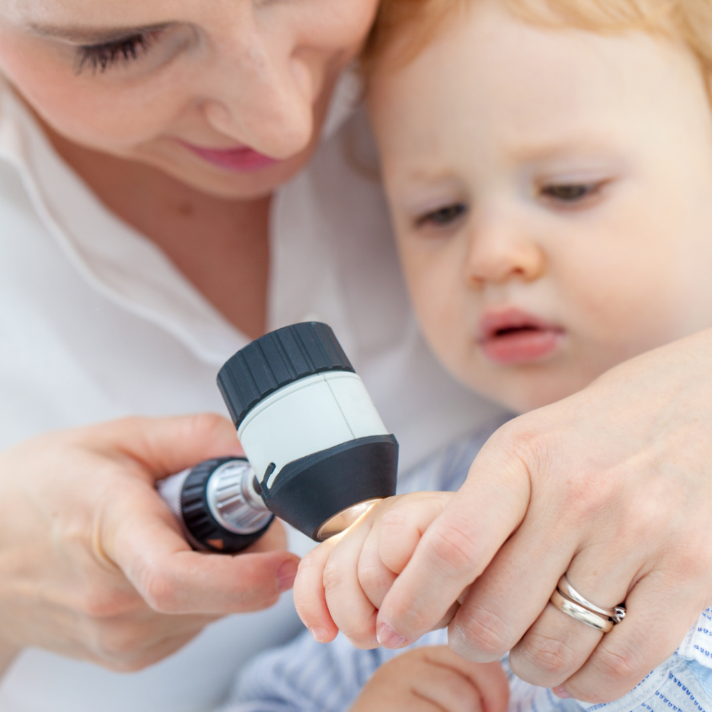 riđokosi dečak sa plavim očima na pregledu kod dermatologa, doktorka pregleda njegovu ruku dermatoskopom zbog sumnje na ekcem