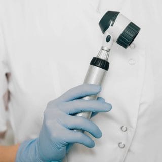 ruka dermatologa u plavoj rukavici drži dermoskop