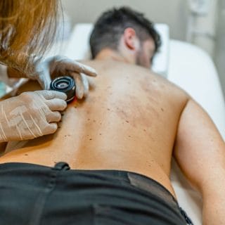 muškarac leži na stomaku u dermatološkoj ordinaciji, a dermatolog pregleda kožu na njegovim leđima