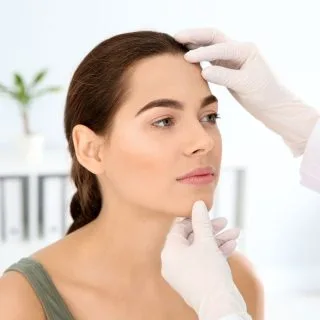 dermatološki pregled ženskog lica u dermatološkoj ordinaciji, ryke dermatologa u belim rukavicama drže lice žene koja je došla da proveri da li ima keratoze