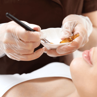 žensko lice i ruke dermatologa iznad njega - u tku je priprema za hemijski piling lica