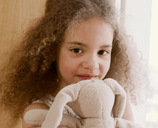 nasmejana kovrdžava devojčica grli plišanog zeku dok čeka da je pregleda dečiji dermatolog