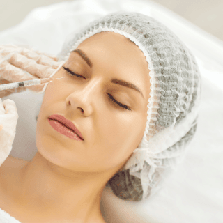 žena zatvorenih očiju leži na stolu u dermatološkoj ordinaciji, a pored njenog lica je špric u kome se nalaze egzosomi